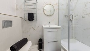 A modern bathroom with a glass shower enclosure, a white sink, and a towel rack.