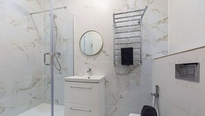 A bathroom with a glass-enclosed shower, a sink with a mirror, a towel rack, and a toilet.