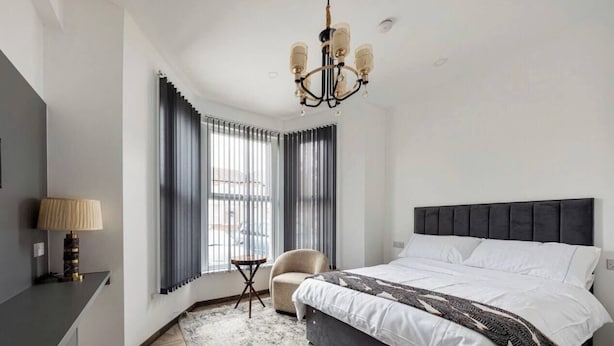 A modern bedroom with a large bed, a chair, a desk, and a chandelier.