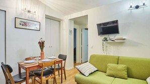 Un espacio habitable compacto con comedor, un sofá verde, un televisor de pantalla plana y una planta pequeña en un estante.
