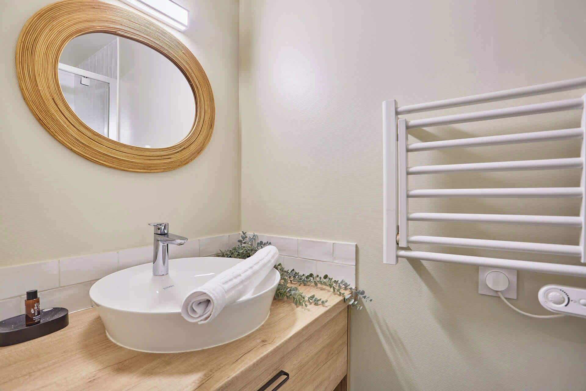Een badkamer met een ronde spiegel, een witte wastafel en een handdoekrek.