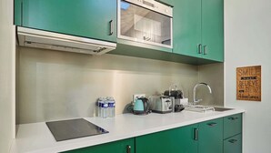 Una cocina con armarios verdes, encimera blanca, tostadora, hervidor y un lavabo.