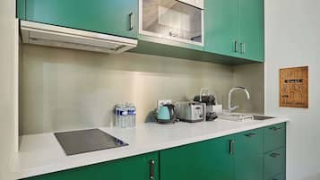Une cuisine avec des meubles de couleur verte, un plan de travail blanc, un grille-pain, une bouilloire et un évier.