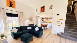 Un salon moderne avec un canapé d’angle vert foncé, une table à manger en bois et un escalier menant à l’étage supérieur.