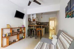A modern living room with a sofa, a bookshelf, and a dining area with stools. - Dreamy Cove, Artistic Hideaway near Floisvos 1BD (Paleo Faliro)