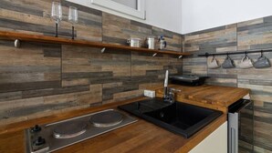 A modern kitchen with wooden countertops, a black induction cooktop, and a built-in dishwasher. - Dreamy Cove, Artistic Hideaway near Floisvos 1BD (Paleo Faliro)