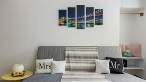 A modern bedroom with a grey sofa bed, striped bedding, and a cityscape artwork on the wall. - Dreamy Cove, Artistic Hideaway near Floisvos 1BD (Paleo Faliro)