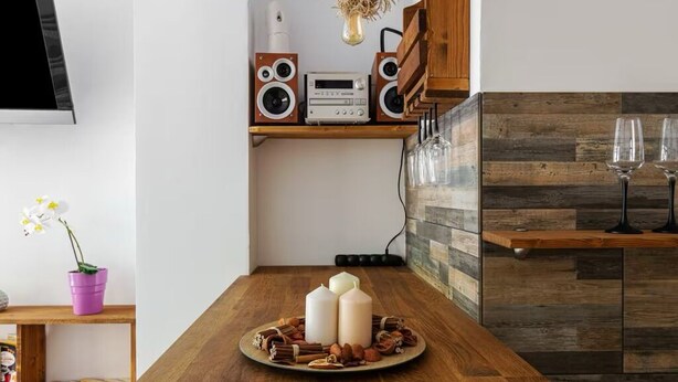 A wooden dining table with a plate of nuts and candles, a speaker system, and a TV mounted on the wall. - Dreamy Cove, Artistic Hideaway near Floisvos 1BD (Paleo Faliro)