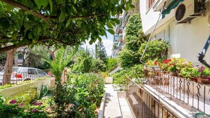 A narrow pathway flanked by lush greenery and potted plants, leading to a building with a metal railing and a visible air conditioning unit. - Dreamy Cove, Artistic Hideaway near Floisvos 1BD (Paleo Faliro)