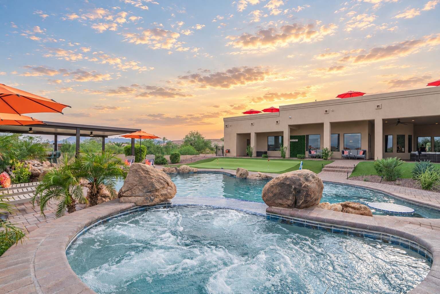 Un espace piscine doté d’un jacuzzi, de gros rochers et d’un coin salon couvert avec des parasols.