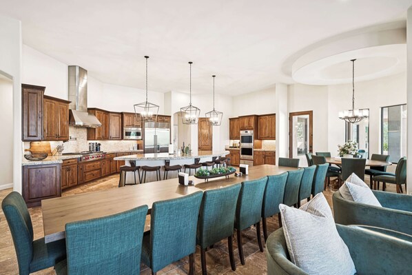 A spacious kitchen with wooden cabinets, a large island, and modern pendant lighting.