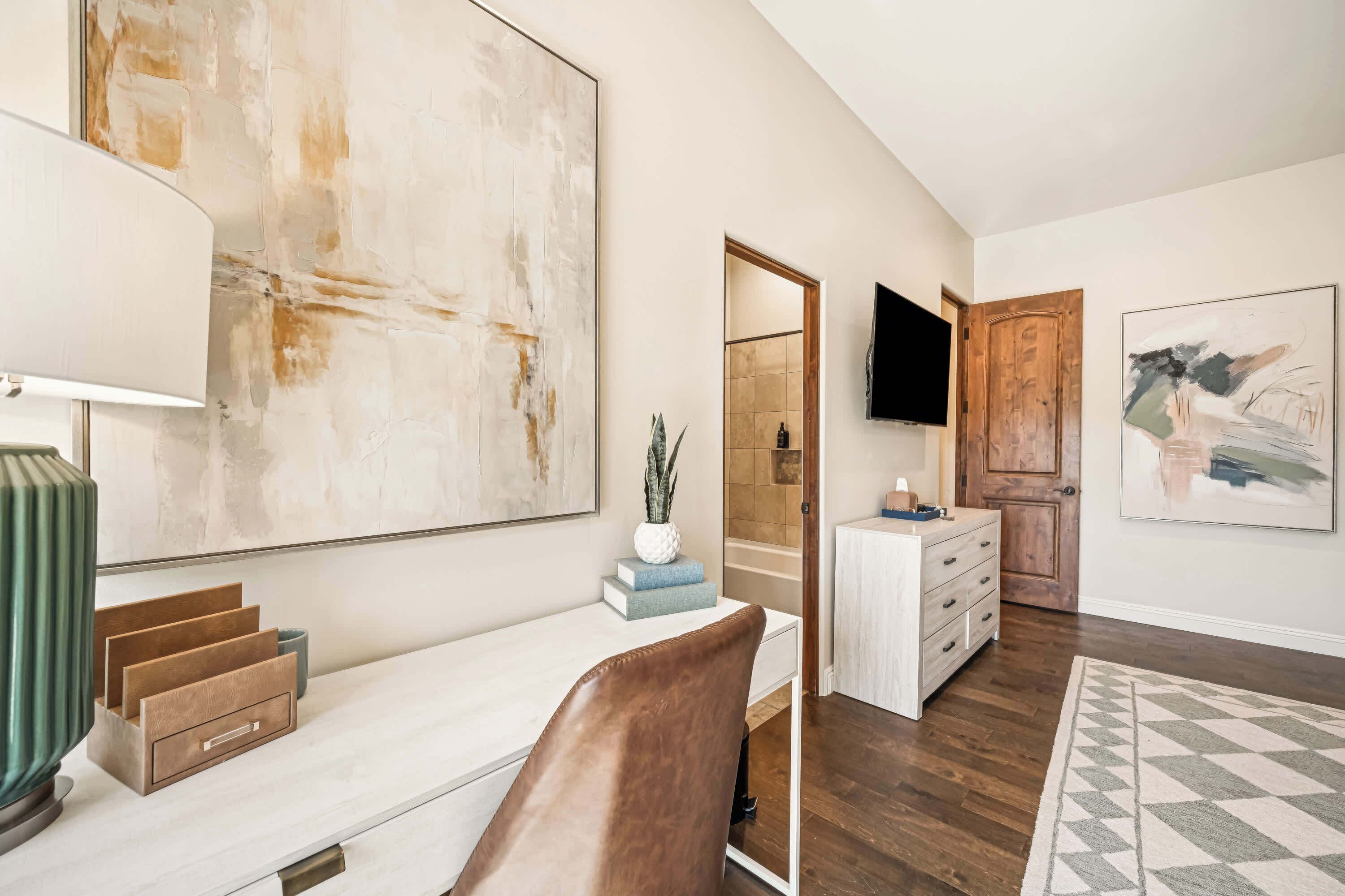 A modern living room with a large abstract painting, a television mounted on the wall, and a wooden door leading to a bathroom.