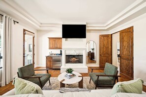 Un salon avec une cheminée, deux fauteuils, une table basse et un téléviseur fixé au mur.