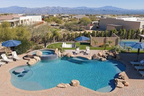 A swimming pool with a hot tub, lounge chairs, and umbrellas.