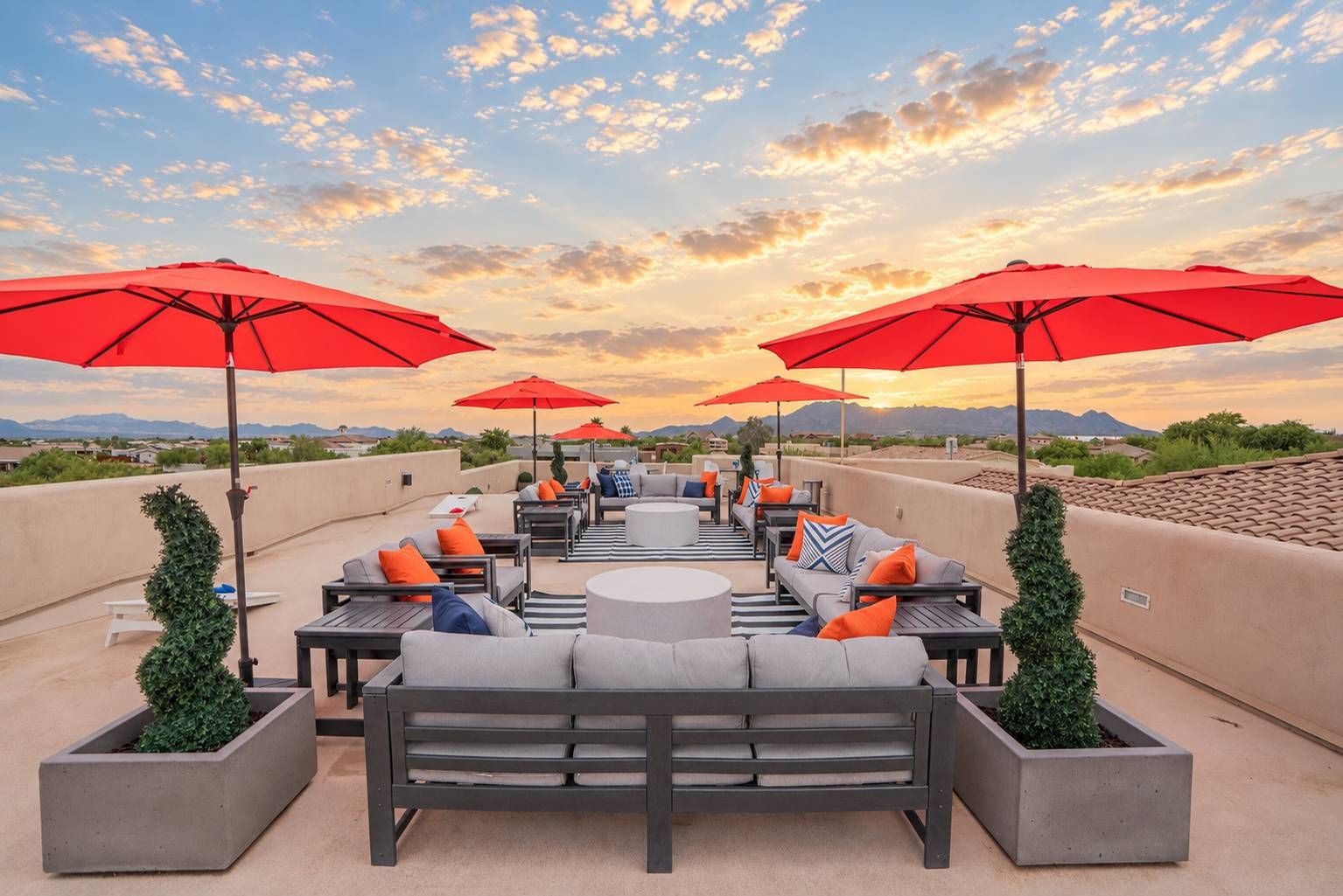 An outdoor patio with multiple seating areas, red umbrellas, and potted plants.