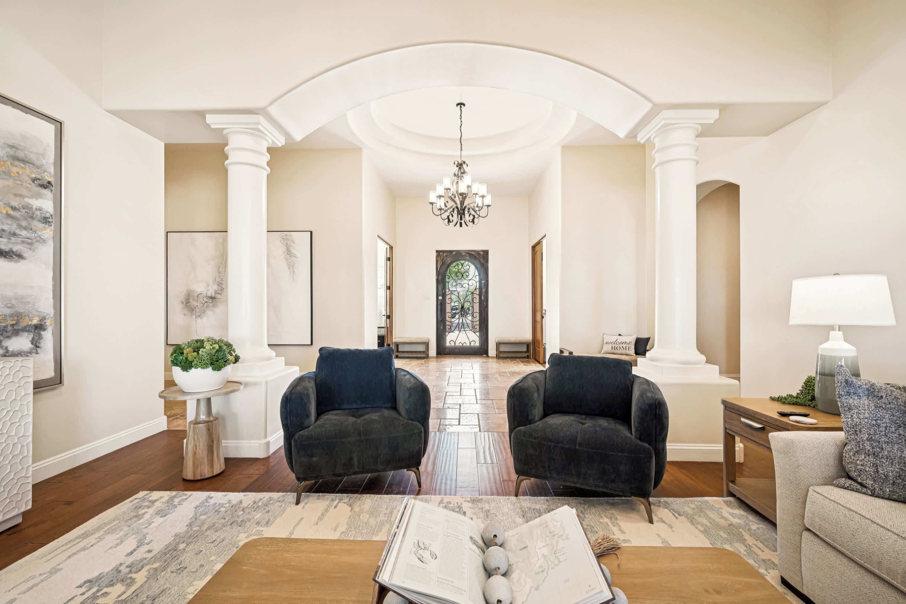 A spacious living room with two dark armchairs, a coffee table with a book, and a lamp on a side table.