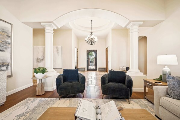 A spacious living room with two dark armchairs, a coffee table with a book, and a lamp on a side table.