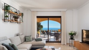 Un salon moderne avec un canapé, une table basse et un meuble pour la télévision. Il y a un balcon avec vue sur la mer.