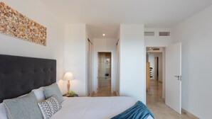 Une chambre d’hôtel avec un grand lit, une tête de lit, une œuvre d’art murale, une lampe de chevet et une vue sur la salle de bain et le couloir.