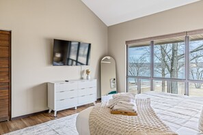 A modern bedroom with a large bed, a TV mounted on the wall, and a view of the outdoors through large windows. - Lionshead Lake Home with Resort Access, Sleeps 11 (Innsbrook)