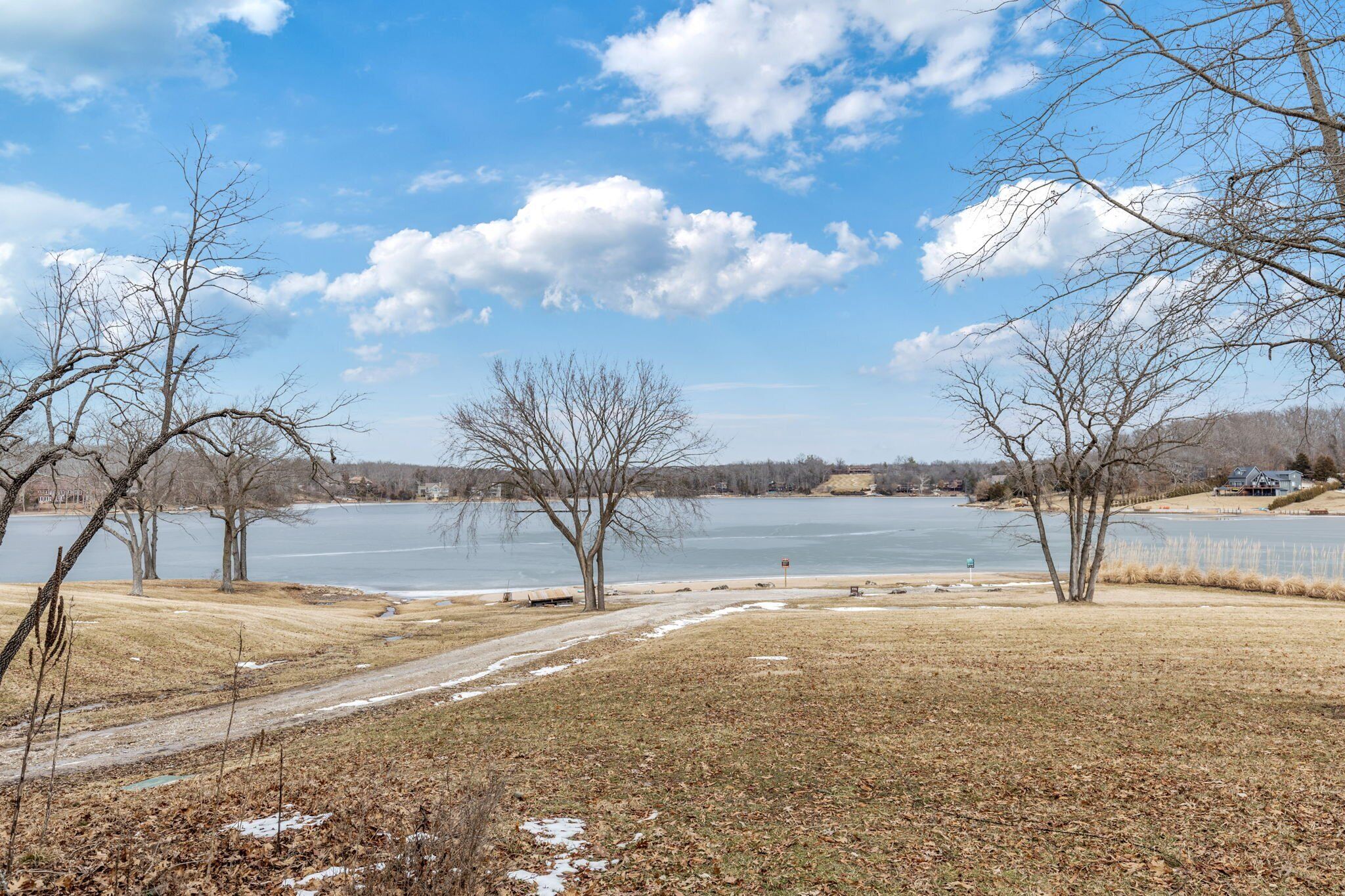 A lakeside view with bare trees, a clear sky, and a distant house.