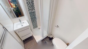 Moderni kylpyhuone, jossa on valkoinen pesuallas, lasinen suihkuseinä ja wc-istuin.