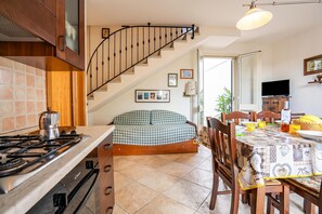 A kitchen with a gas stove, wooden cabinets, a checkered sofa, a dining table with chairs, and a staircase. - Casa Machiavelli Near The Sea (Porto Cesareo)
