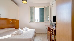 A hotel room with a bed, a desk, a television, and a window with open shutters. - Casa Machiavelli Near The Sea (Porto Cesareo)