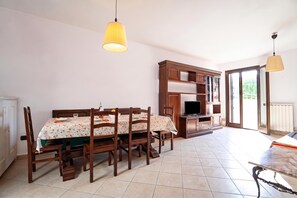Ein Essbereich mit einem Tisch für vier Personen, einem Fernseher auf einem Schrank und einer Glastür zum Balkon.