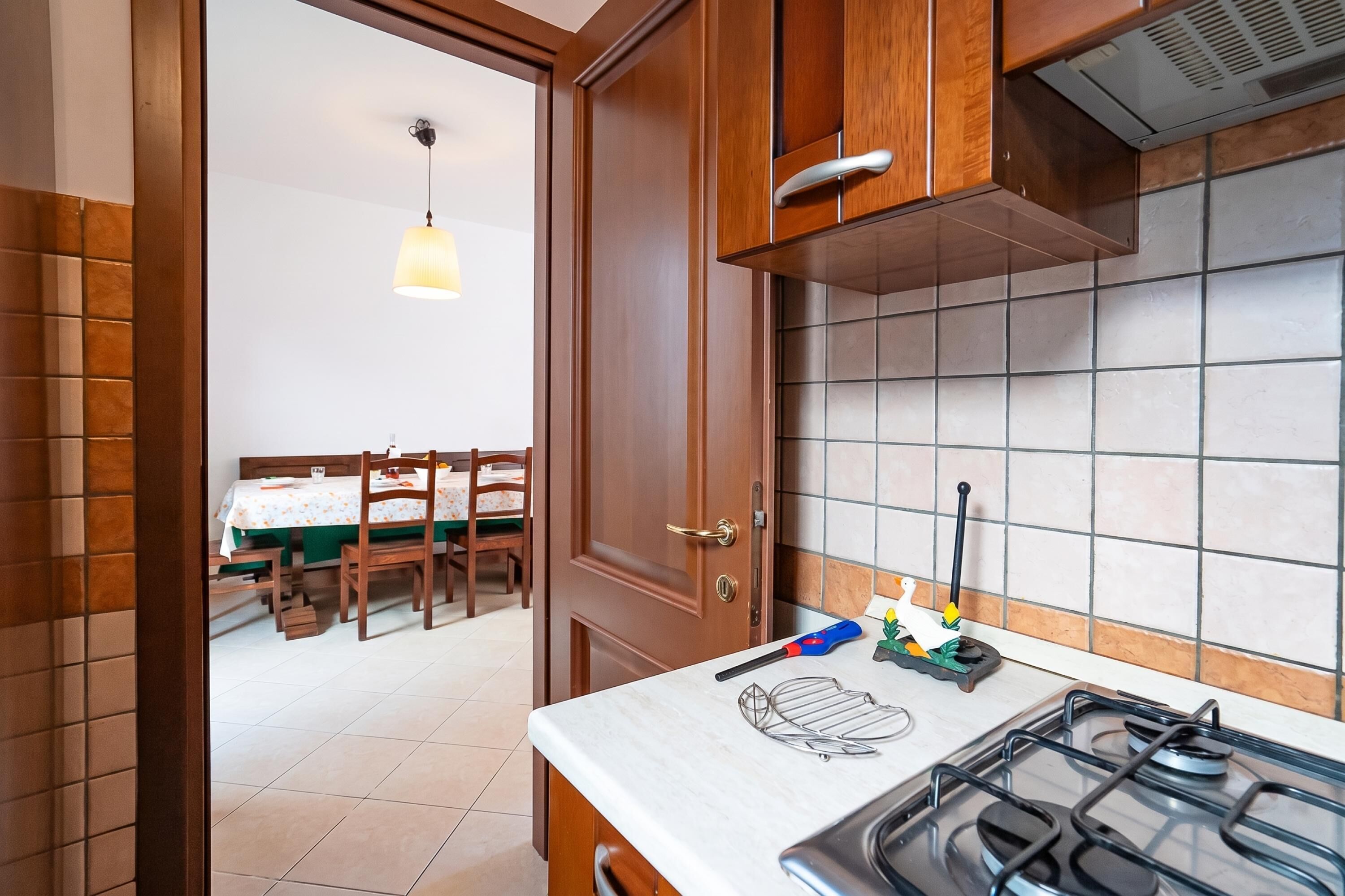 Une cuisine équipée d’une cuisinière à gaz, de meubles en bois, d’un plan de travail carrelé et d’un coin repas avec une table et des chaises.