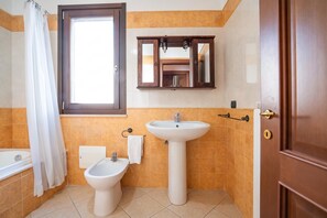 Ein Badezimmer mit Badewanne, Bidet, Waschbecken und einem Fenster mit Vorhang.