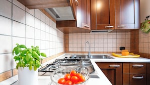A kitchen with wooden cabinets, a gas stove, a sink, and a bowl of tomatoes. - Casa Pascoli With Veranda Dining Near Sandy Beach (Porto Cesareo)