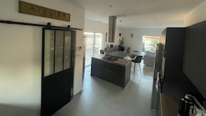Una cocina moderna con una isla central, un comedor y una puerta visible con la etiqueta 'ATELIER'.