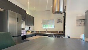 Una cocina moderna con una isla central, electrodomésticos de acero inoxidable y un amplio ventanal con persianas.