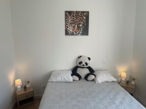 A bedroom with a bed, a panda plush toy, a leopard painting, bedside lamps, and a nightstand.