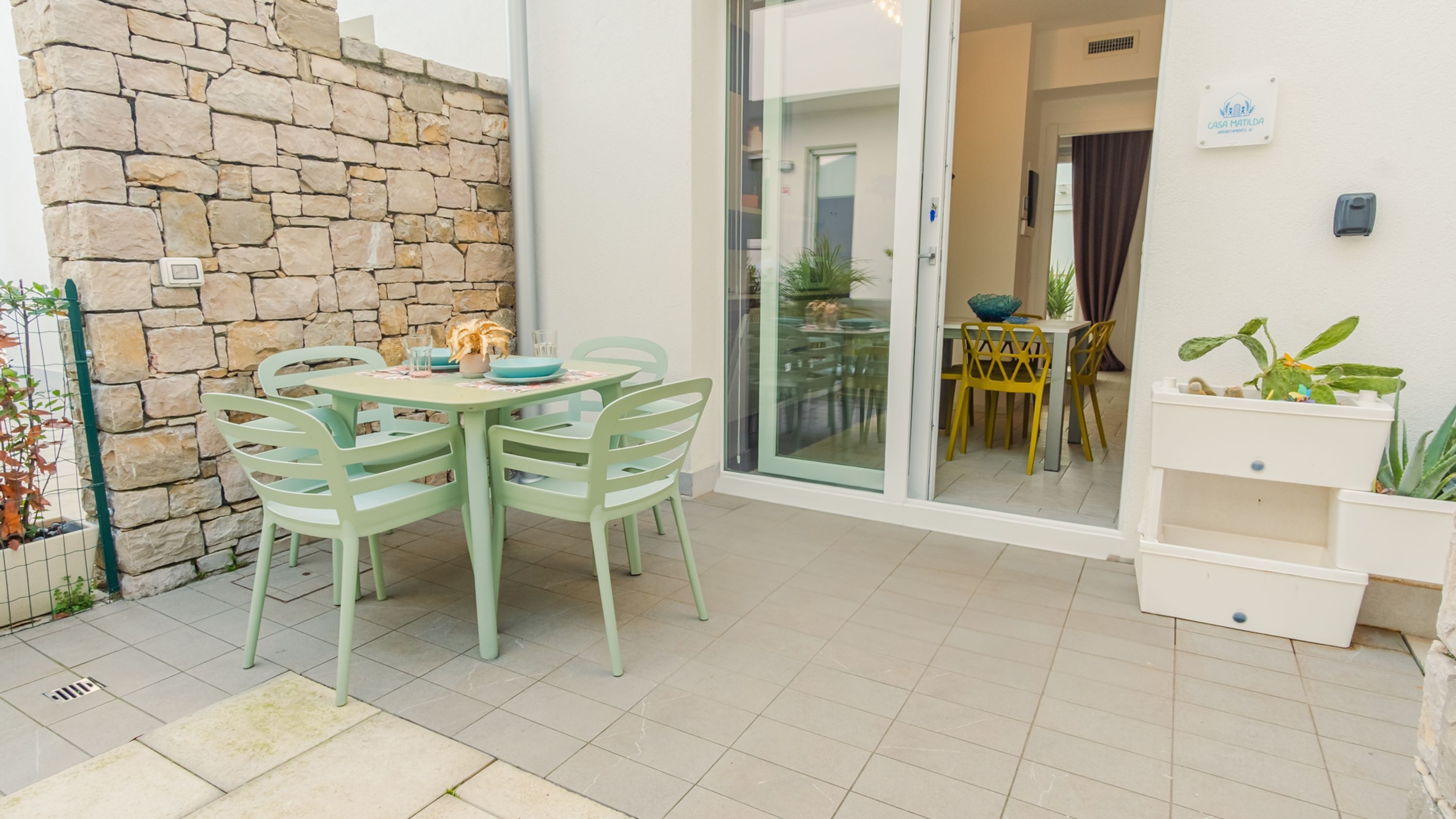 A patio with a stone wall, a table with chairs, and a sliding glass door leading to an interior dining area.