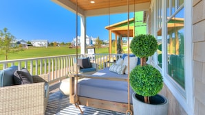 A covered porch with wicker furniture, a ceiling fan, and a view of houses in the background. - Carlton Landing-Shingle Ready to Mingle (Carlton Landing)