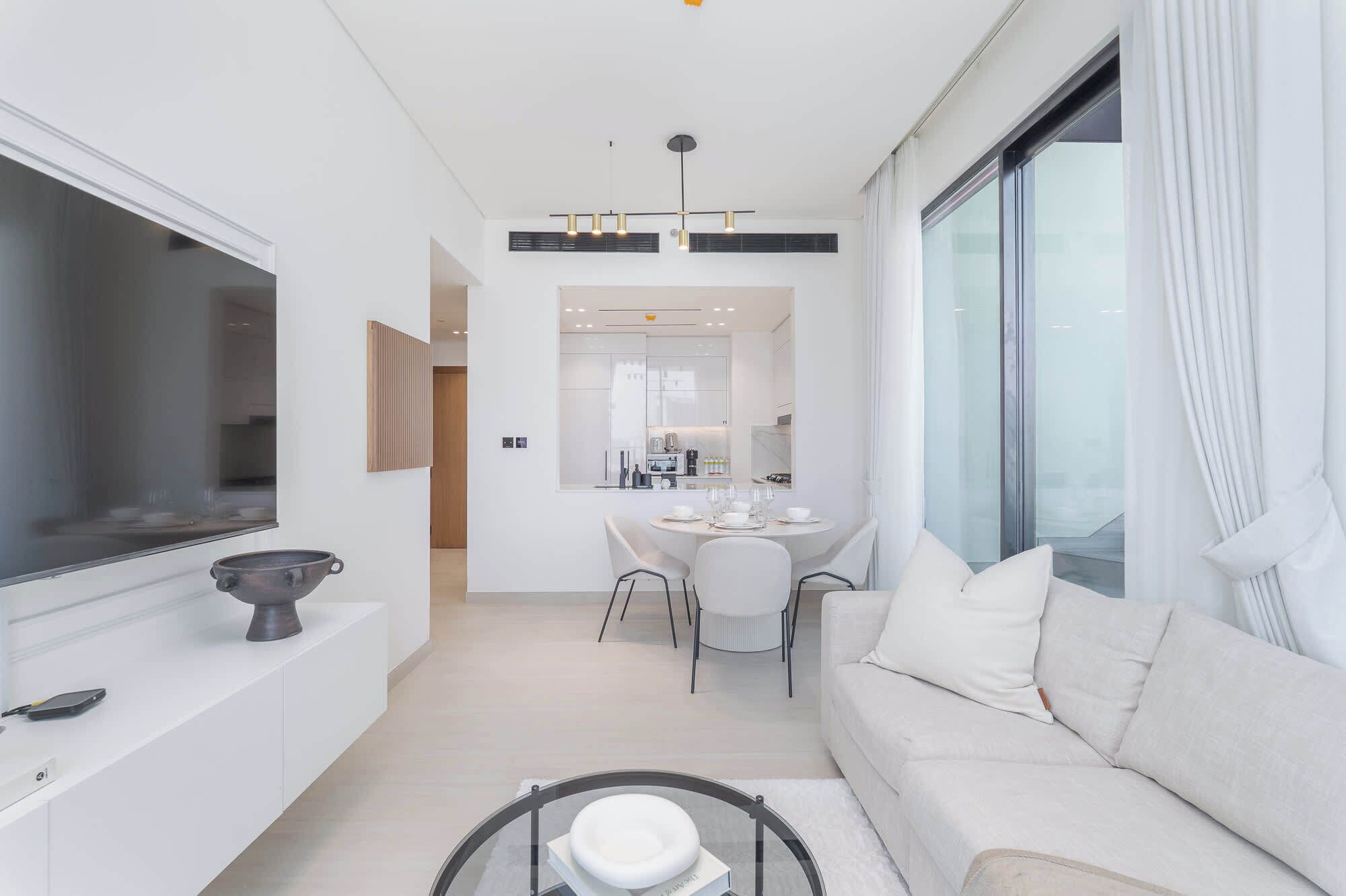 Een moderne woonkamer met een bank, een eethoek met een tafel en stoelen, en een keuken op de achtergrond.
