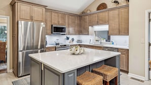 Una cocina con armarios de madera, electrodomésticos de acero inoxidable, una isla central y taburetes de mimbre.