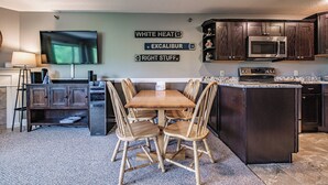 A modern kitchen with dark wooden cabinets, a built-in microwave, and a dining area with a wooden table and chairs. - Two bedroom North Peak Condo (Newry)