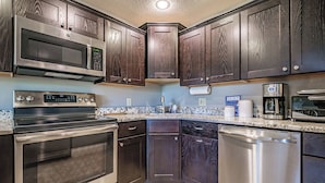 A modern kitchen with dark wood cabinets, stainless steel appliances including a microwave, oven, and dishwasher, and a granite countertop. - Two bedroom North Peak Condo (Newry)