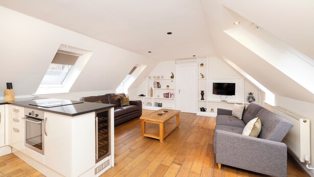 A spacious loft apartment with a kitchen, dining area, and living room. It features a loft bed, a gray sofa, and a wooden coffee table. - JOIVY Modern flats near Edinburgh Castle (Edinburgh)