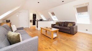 A spacious living area with a grey sofa, a brown leather sofa, and a wooden coffee table. There is a kitchen in the background with white cabinets and a microwave. - JOIVY Modern flats near Edinburgh Castle (Edinburgh)