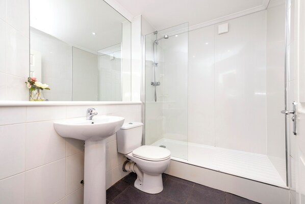 Une salle de bain moderne avec un lavabo blanc, des toilettes et une douche à parois de verre.
