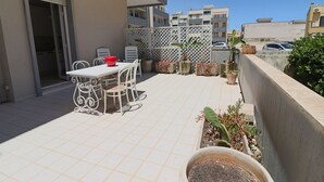 Un patio al aire libre con mesa y sillas, plantas en macetas y vistas de edificios cercanos.
