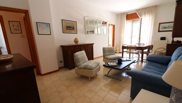 Una sala de estar con un sofá, dos sillones, una mesa de centro, una mesa de comedor con sillas, un aparador y un espejo.