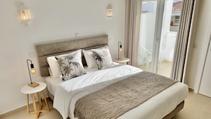 A spacious bedroom with a large bed, two nightstands, a round side table, and a view of a balcony.