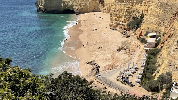 A coastal beach with rocky cliffs, a sandy shore, and a few beach umbrellas.