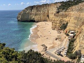 A coastal beach with rocky cliffs, a sandy shore, and a few beach umbrellas. - Casa Amira (Colina Branca 14) (Carvoeiro)