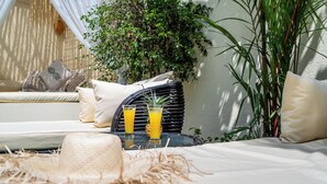 En solig uteservering med en flätstol, en bekväm soffa och två glas apelsinjuice på ett bord.